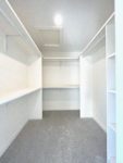 An empty white primary walk-in closet with shelving and rods.