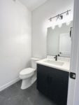 A powder room showing a white toilet sitting next to a bathroom sink cabinet.