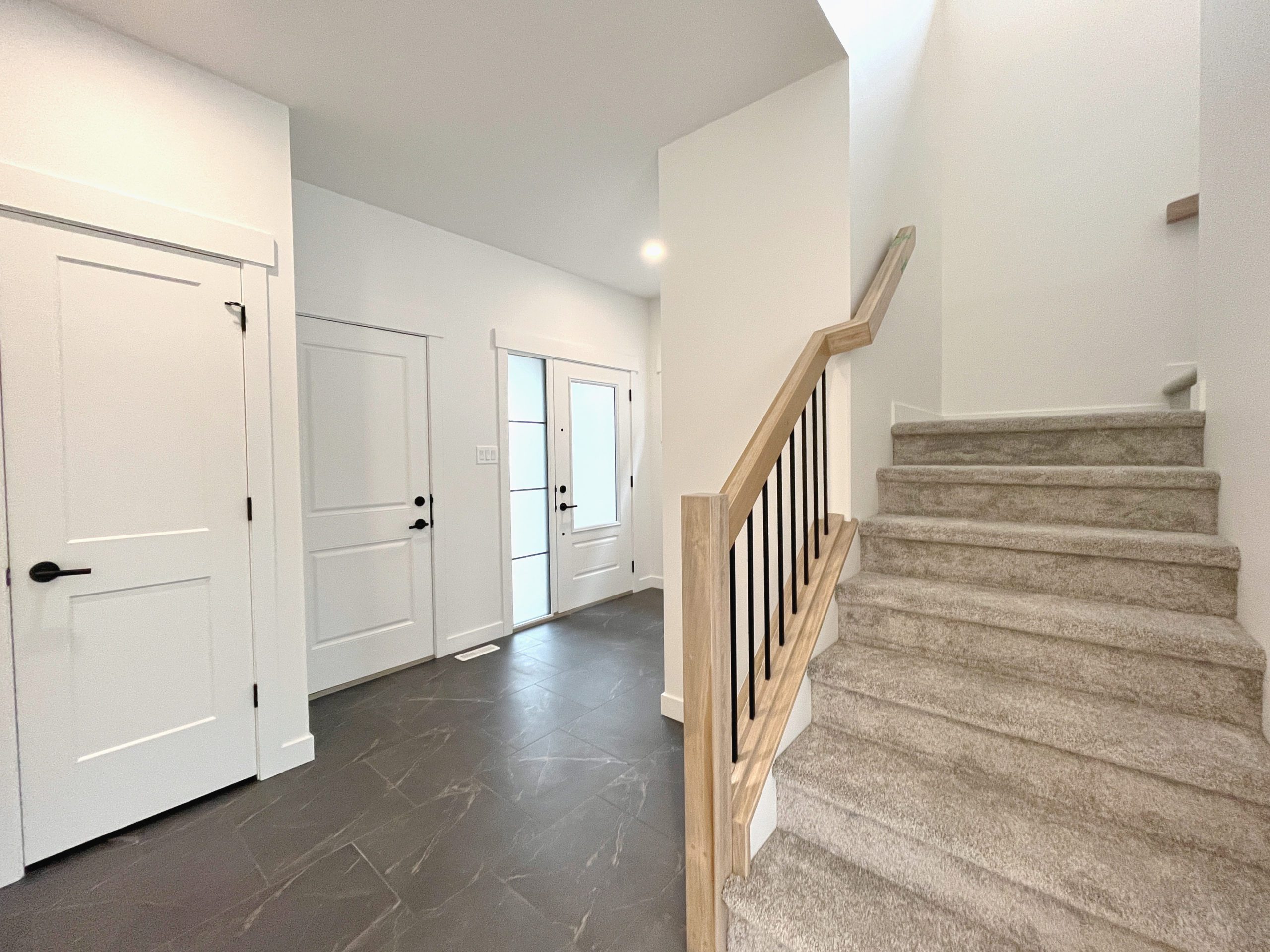 A staircase leading upstairs with carpet and the entryway to garage and front door with tiled flooring.
