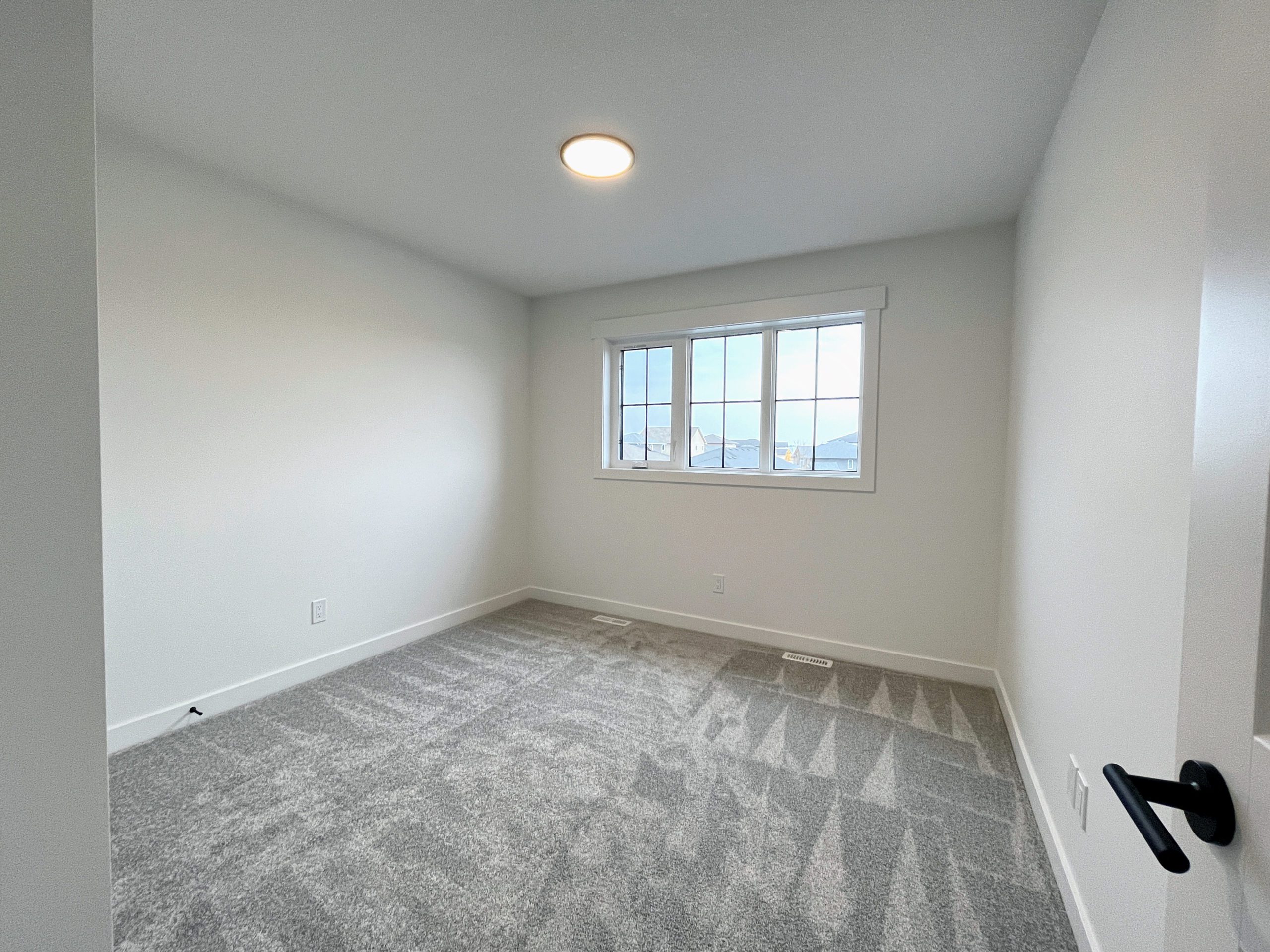 An empty room with a flat profile ceiling fixture with a carpeted floor and a window.