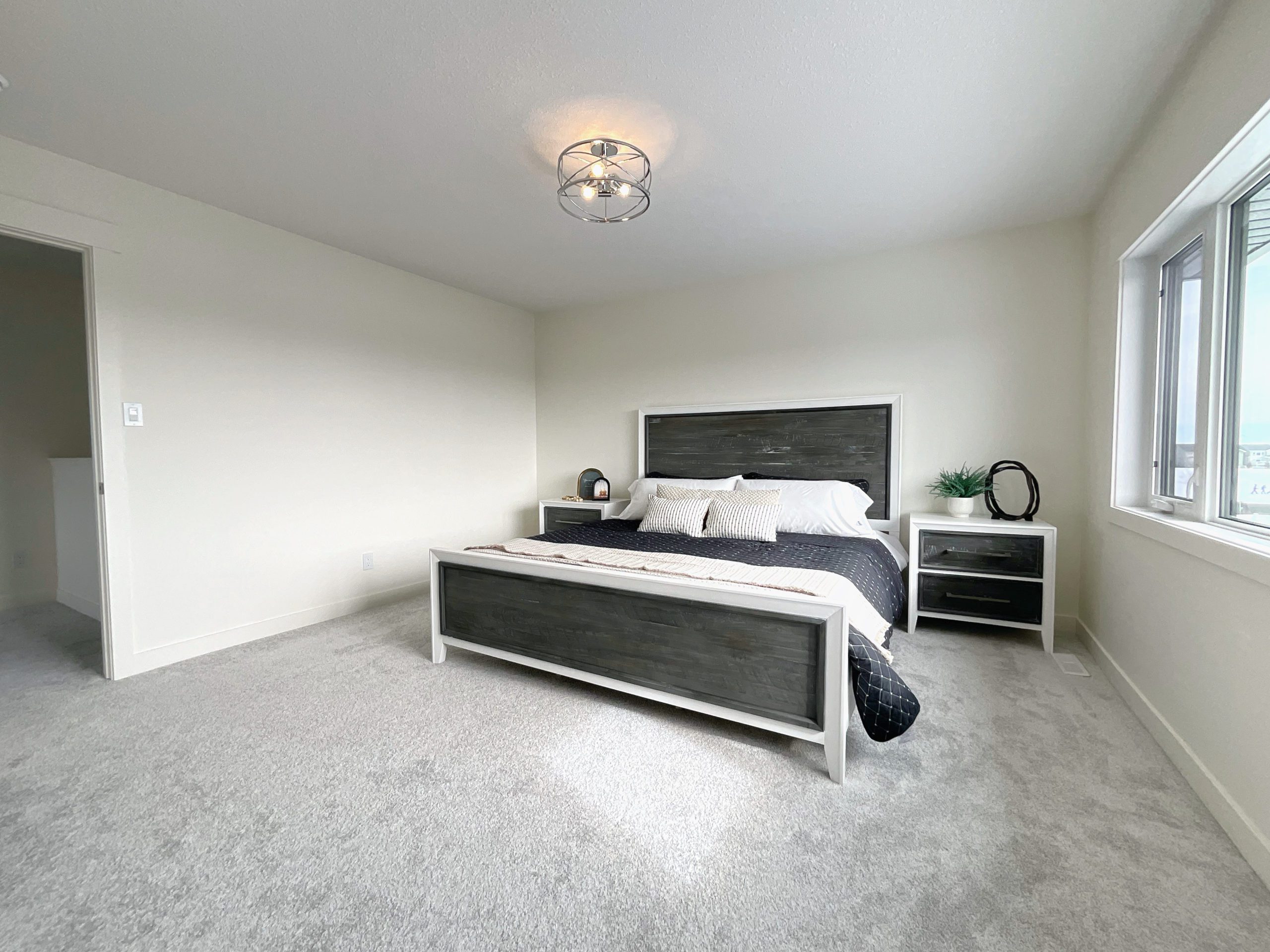 A primary bedroom with a king bed, nightstands, semi-flush light fixture and a large window.