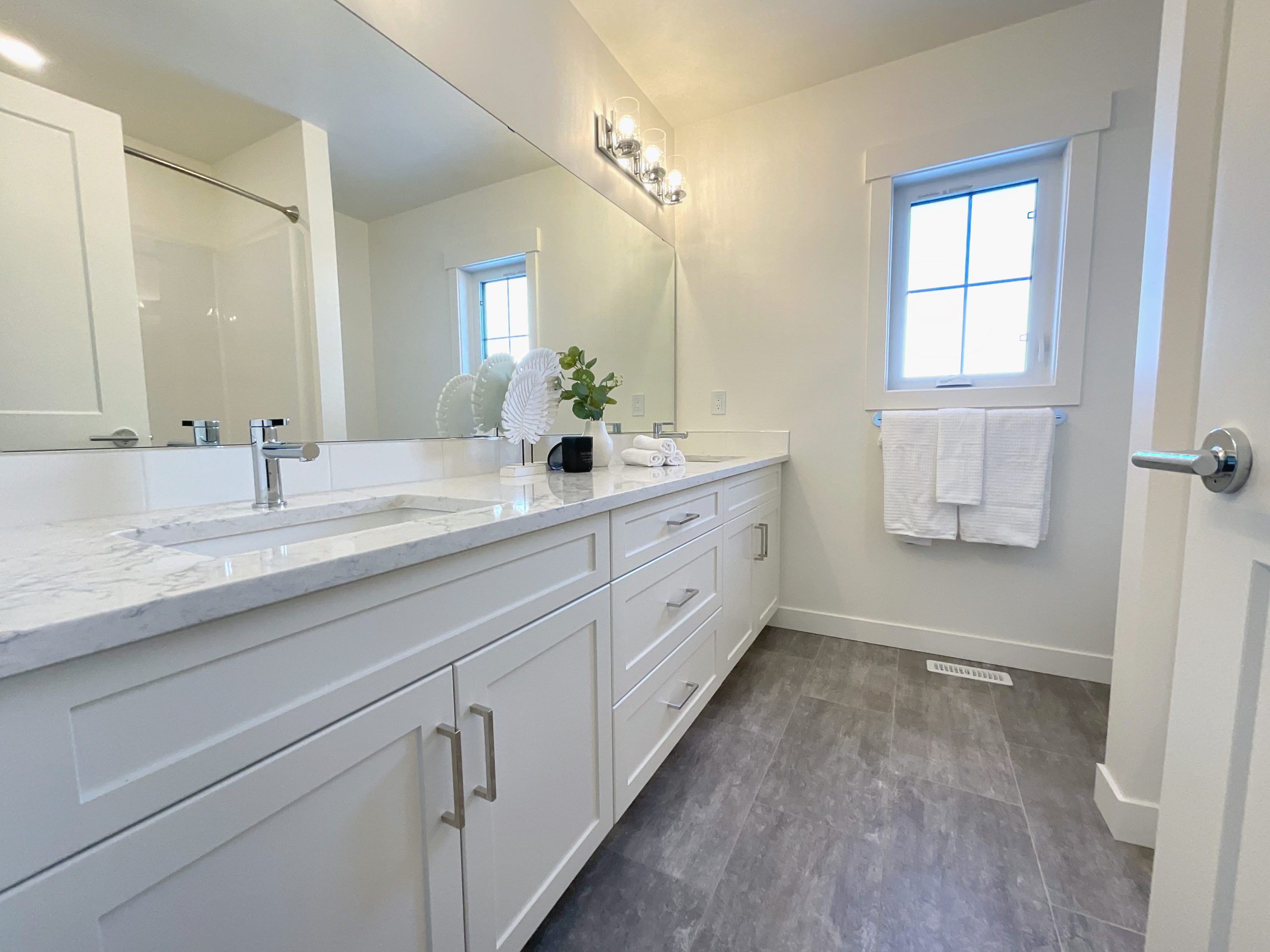 A white family bathroom with a large mirror and double sinks.