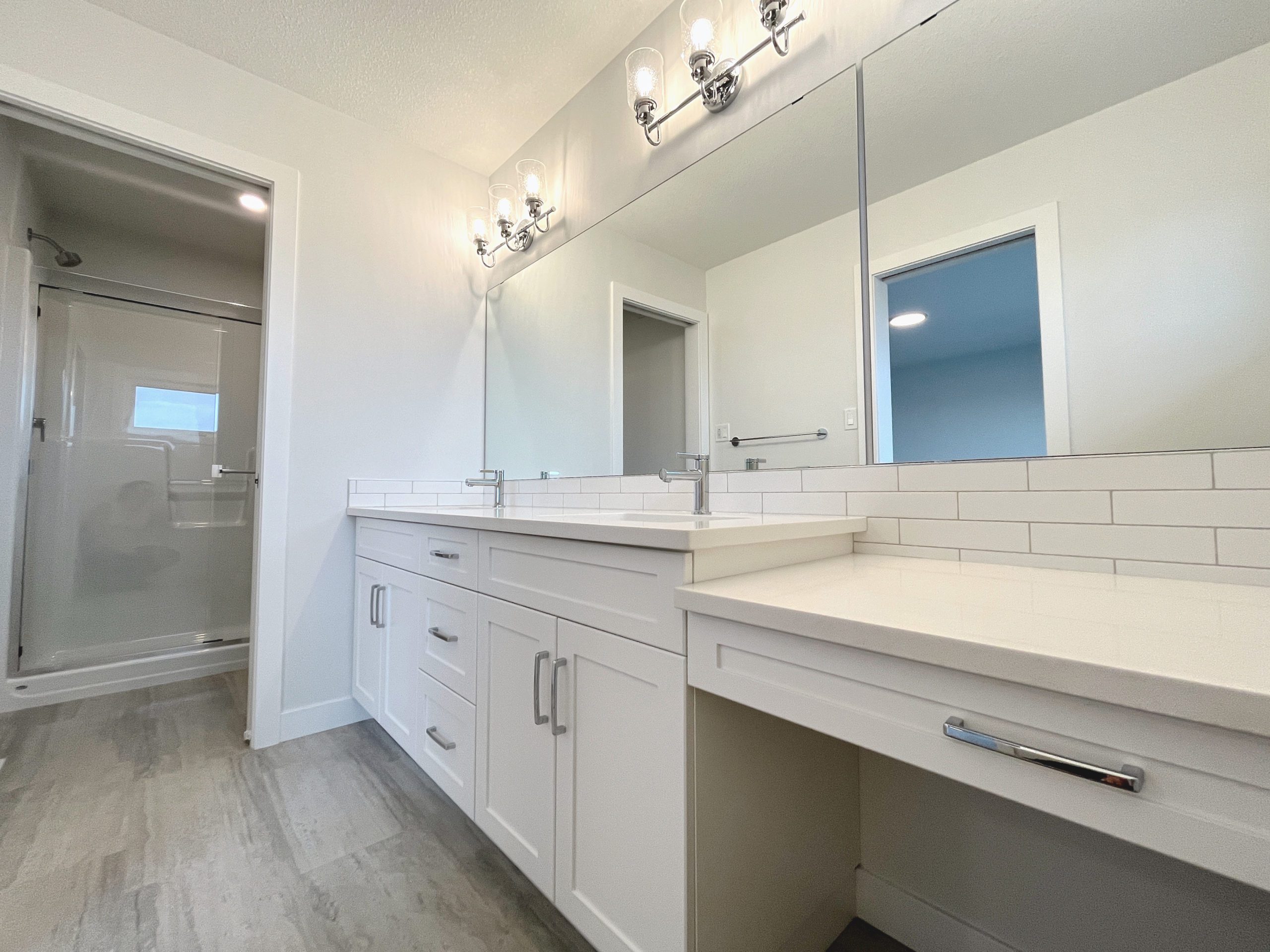 Primary bathroom with double sinks, makeup counter and a large mirror, shows door to water closet.