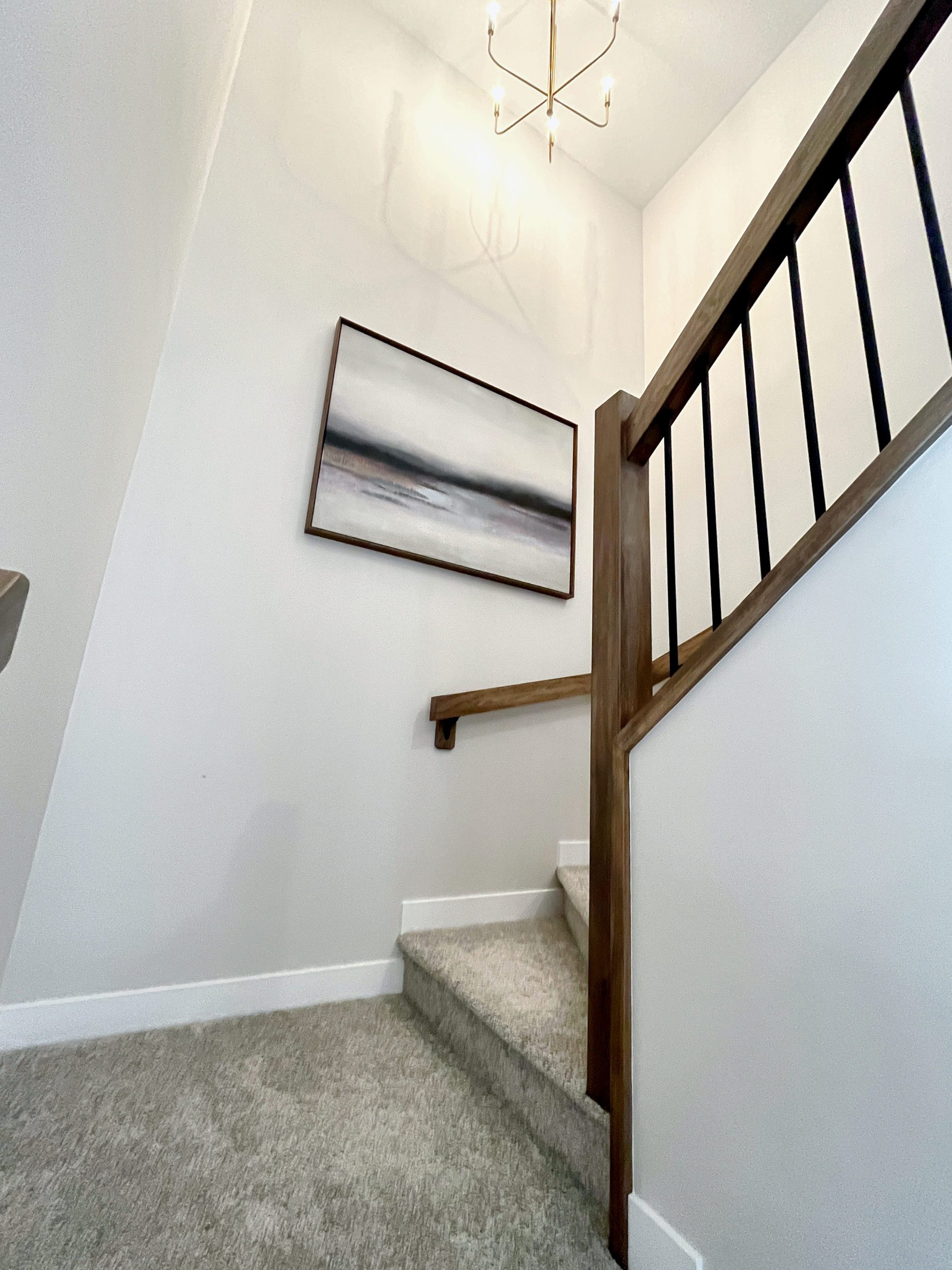 Shows the stairwell to the second level with picture hanging on a wall and chandelier above.