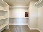 Shows primary walk in closet with white shelving and rods.