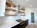 Shows close up of kitchen slide-in range and range hood with exposed shelving.