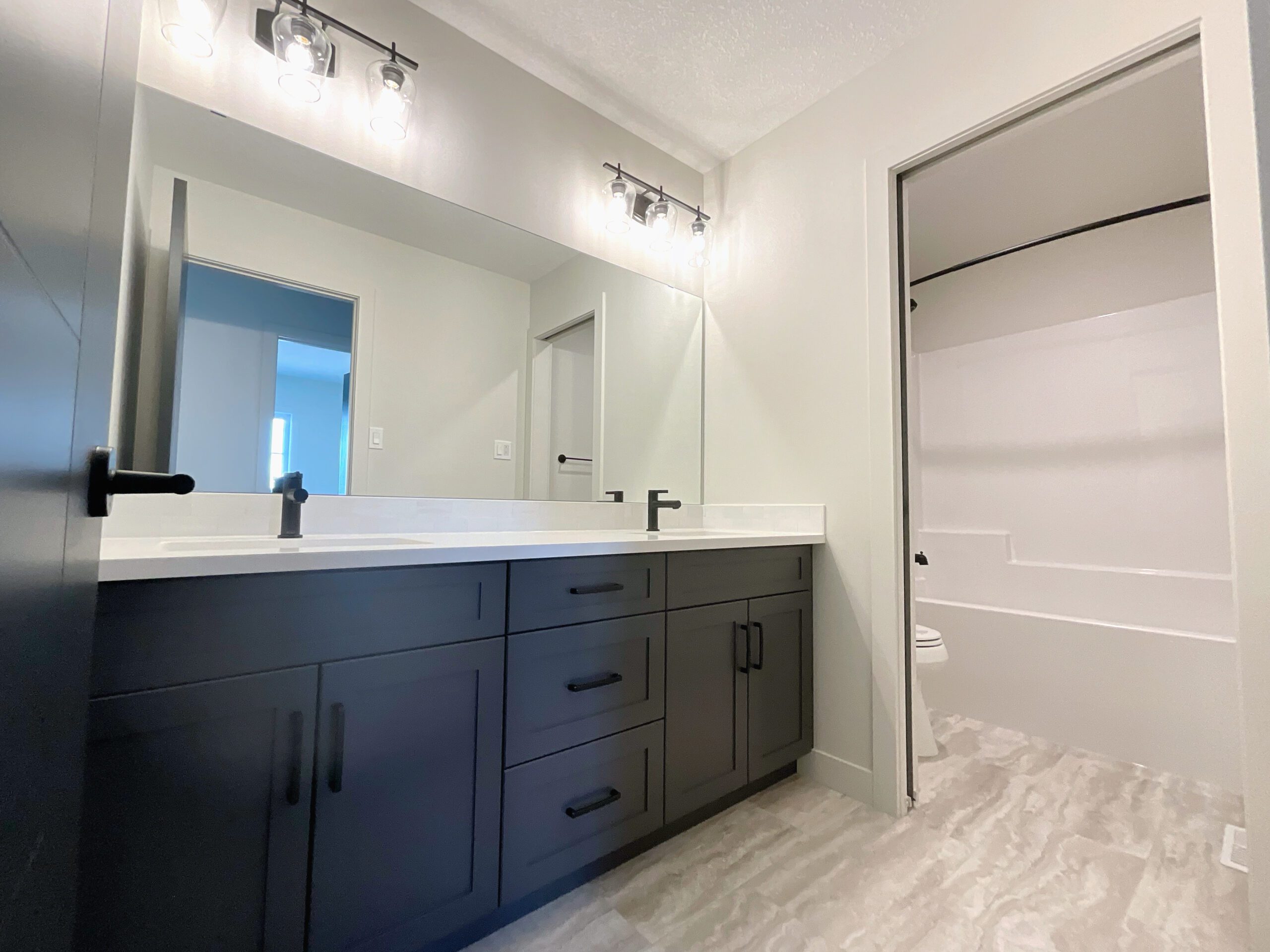 A family bathroom with a large mirror and double sinks with seperate water closet with toilet and combination tub shower.