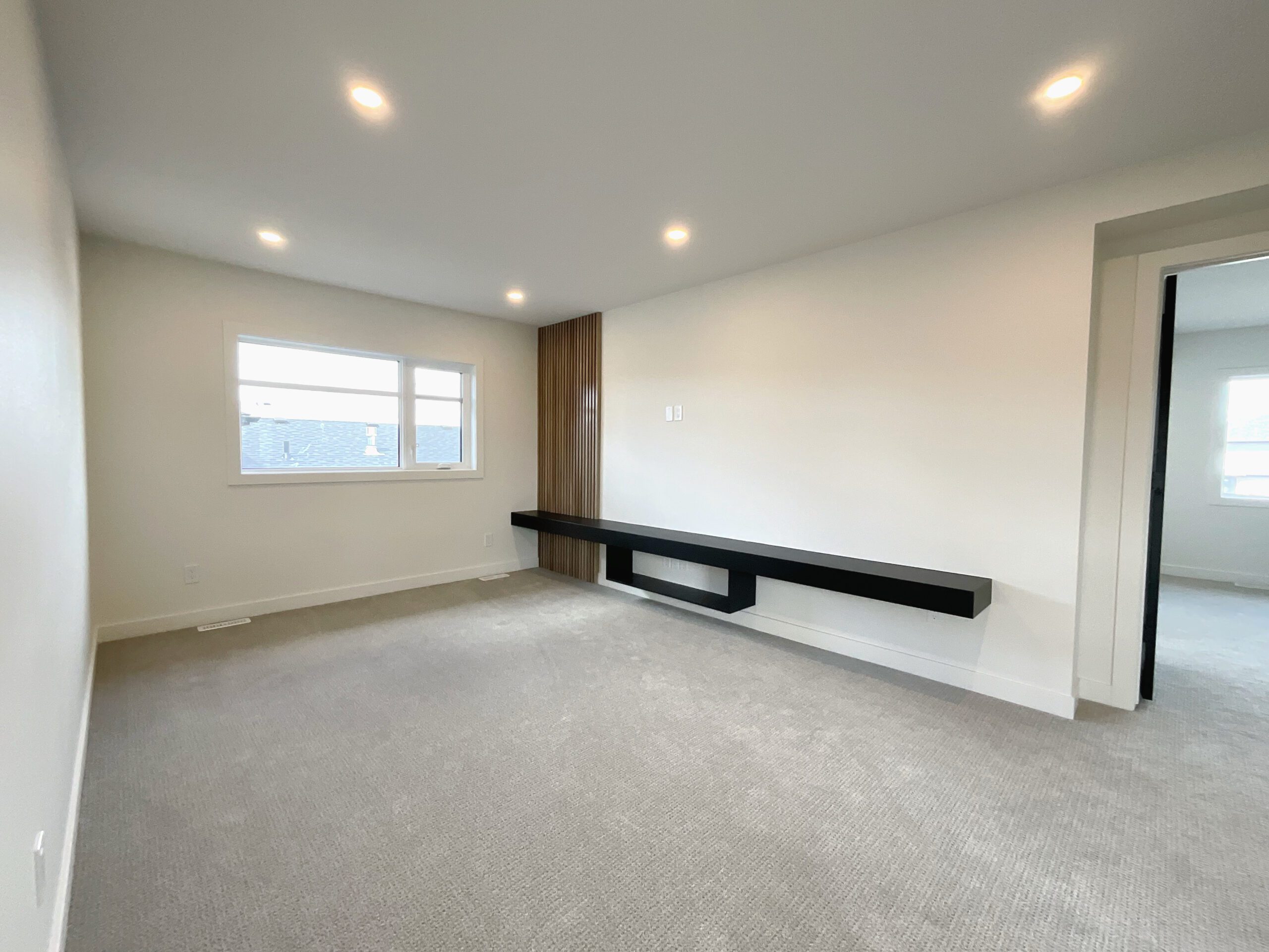An empty bonus room with a built-in media console and decorative wood trim with carpet on the floor.