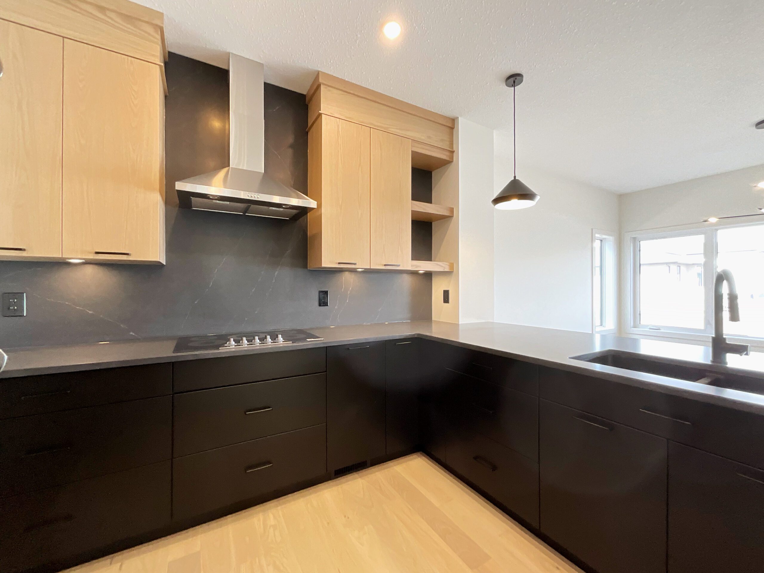 A kitchen with wooden upper cabinets and black lower cabinets with a marbled charcoal quartz counter tops which also serves as a backsplash which runs up the wall behind the range and range hood.