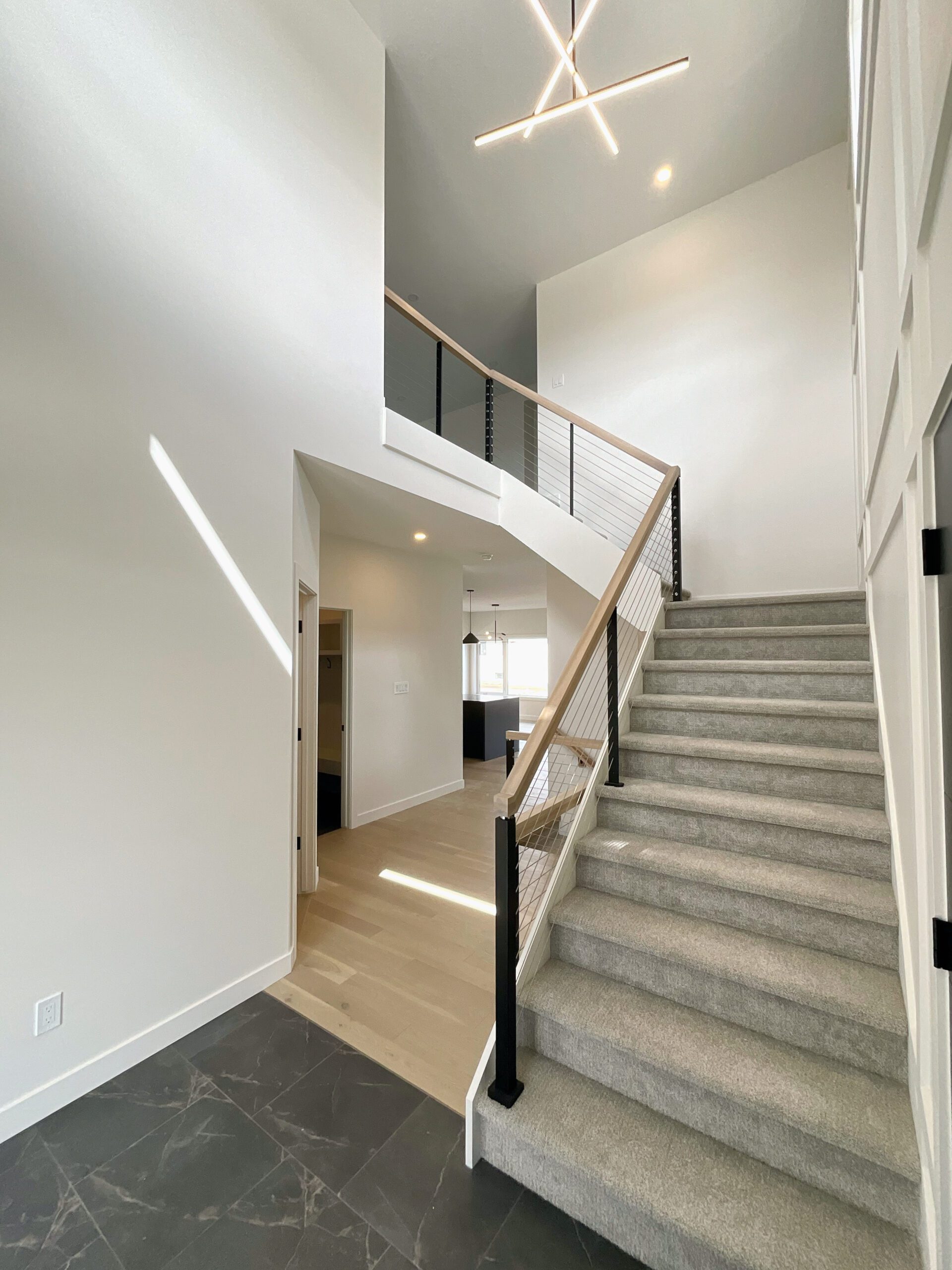 The staircase leading up to a second story with cable railing and large modern chandelier.
