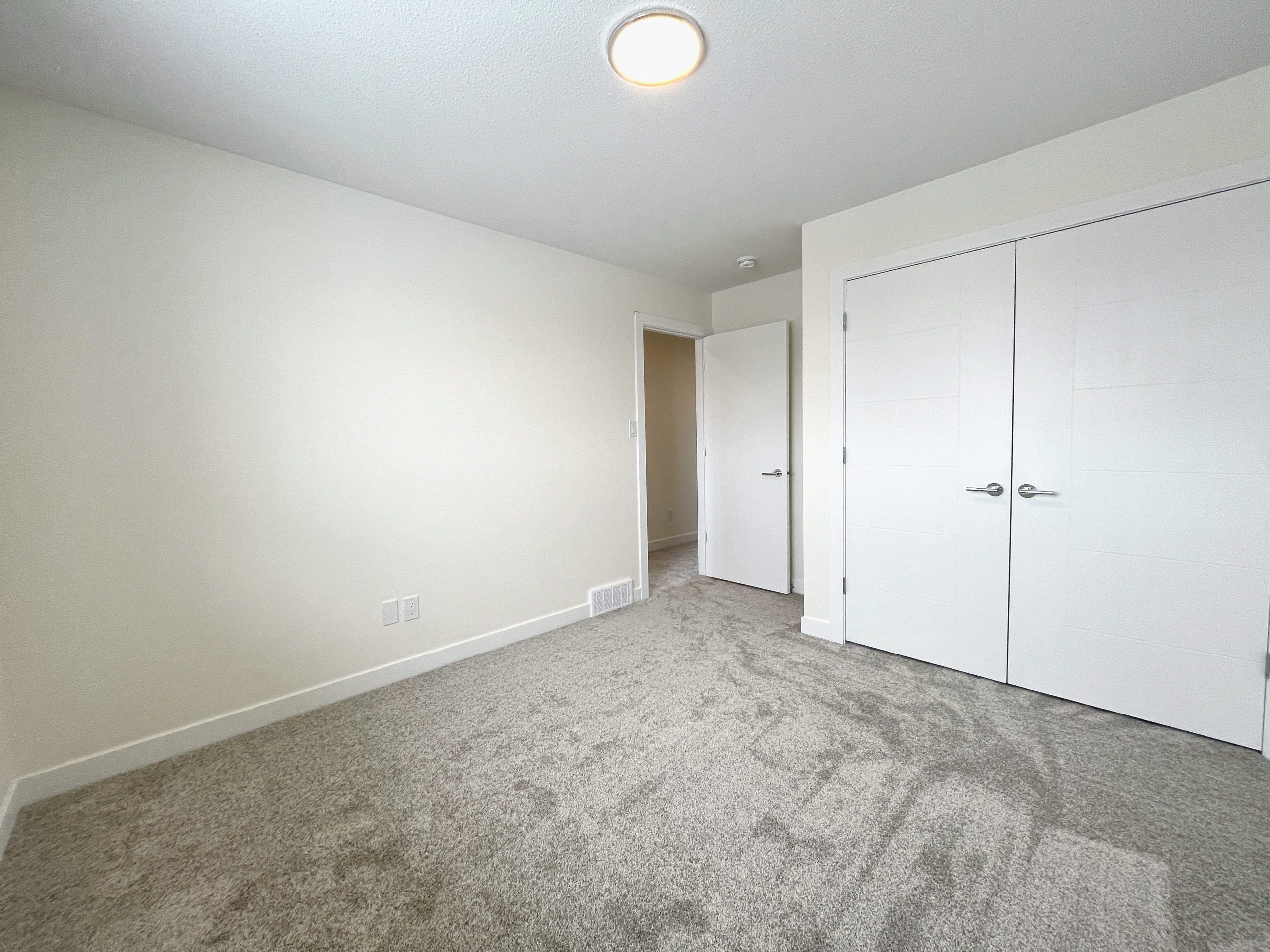 An empty bedroom showing the door to the hallway and closet.