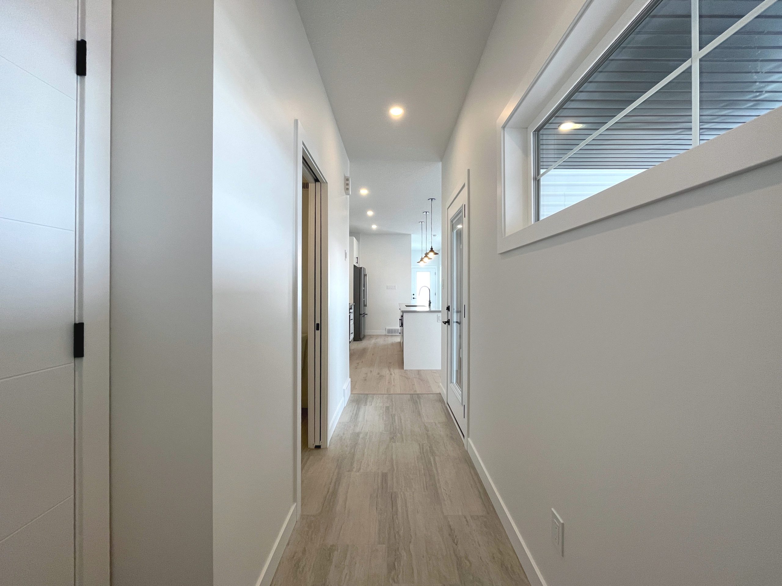 A white hallway to the garage and covered deck with vinyl floors and windows.