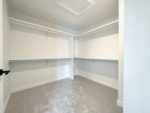 An empty primary walk-in closet with shelving, rods, white walls and carpet flooring.
