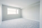An empty room with white carpet and a window.