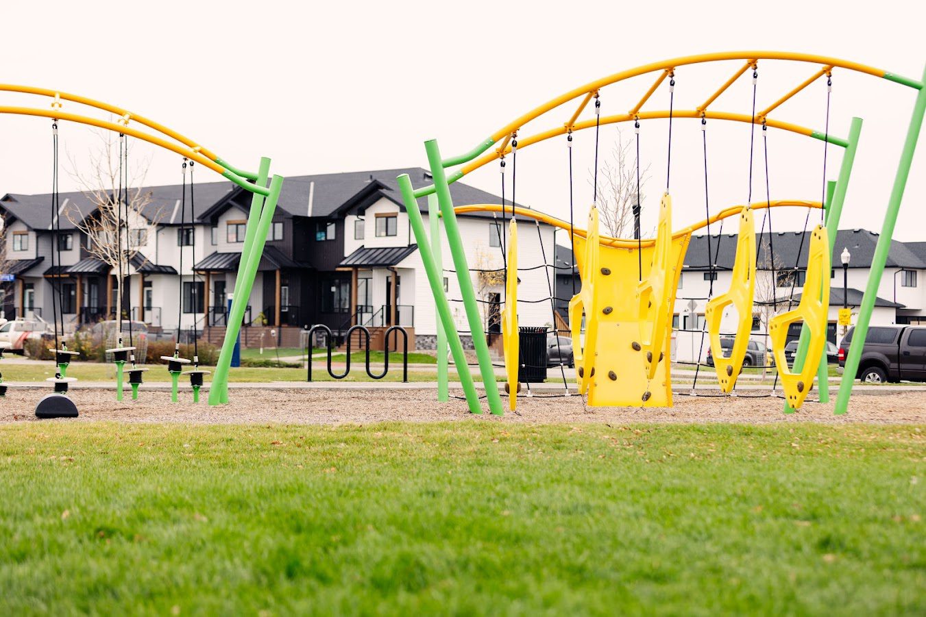 A playground with green and yellow swings in front of a house.