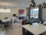 A modern open-plan living space in a two-storey home in Pilot Butte, featuring a dining area, kitchen, and lounge with contemporary furnishings and a fireplace.