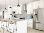 A white kitchen with stainless steel appliances and stools.
