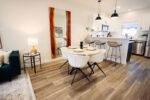 Modern open-concept kitchen and dining area with a round table, white chairs, a large mirror, pendant lights, and a breakfast bar with stools.