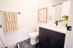 A modern bathroom with a white sink, dark vanity, striped towels, rainbow artwork, and black fixtures.