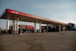 A Co-op gas station with multiple fuel pumps under a large canopy, a few vehicles parked, and a clear sky in the background.